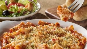 bowl of five cheese ziti pasta on a table with salad and breadsticks in the background